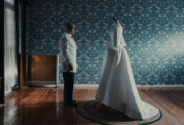 Balenciaga en un momento de la serie delante de un vestido de novia.