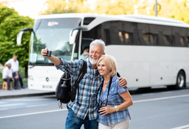 Pareja de abuelos tomándose un selfie delante de un autocar
