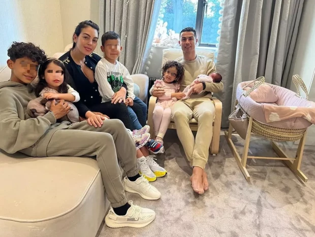 Georgina Rodríguez y Cristiano Ronaldo posando sentados en el sofá de su casa con sus hijos