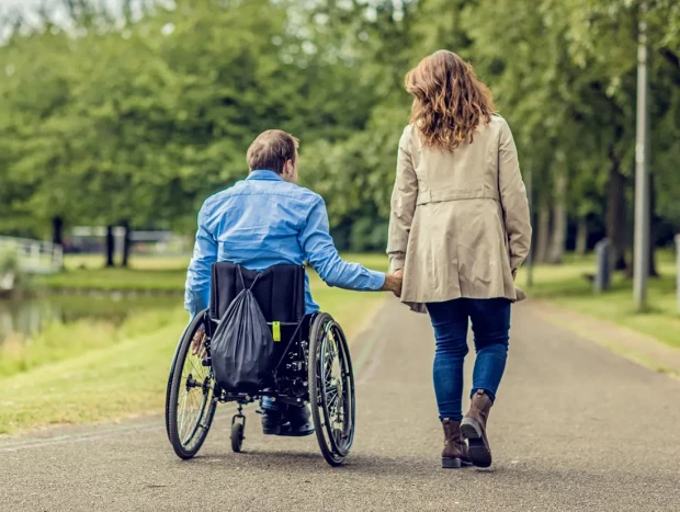 Pareja paseando por un parque. El hombre va en silla de ruedas.