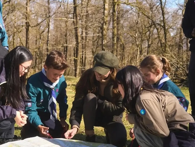 Kate Middleton mirando un mapa junto a unos jóvenes scouts en un bosque.