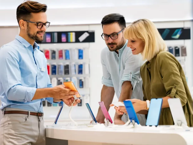 Vendedor de móviles hablando con clientes en una tienda de electrónica.