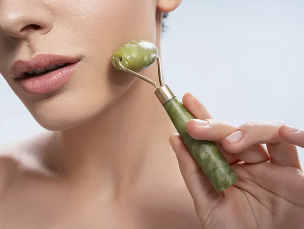 Mujer con un roller de jade haciéndose un masaje facial.