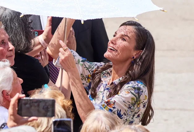 La reina Letizia mirando la sombrilla de una señora.