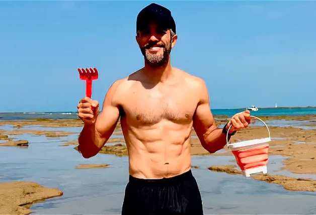 Roberto Leal con un rastrillo y un cubo en la playa.