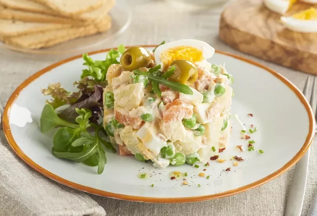 Ensaladilla rusa casera con patatas, zanahorias, guisantes y mayonesa, lista para servir como tapa o entrante refrescante.