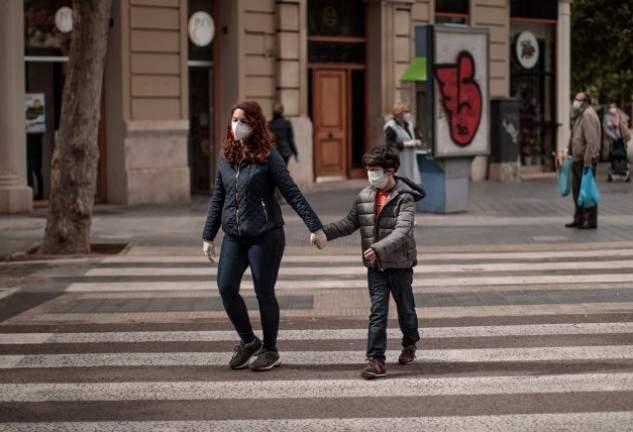 Una madre cruza la calle con su hijo menor de edad, ambos protegidos con mascarillas.