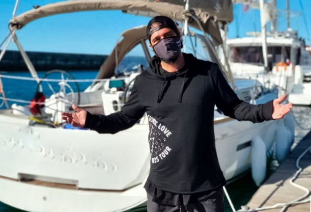 Antonio Orozco posando con mascarilla frente al velero con el que está navegando.