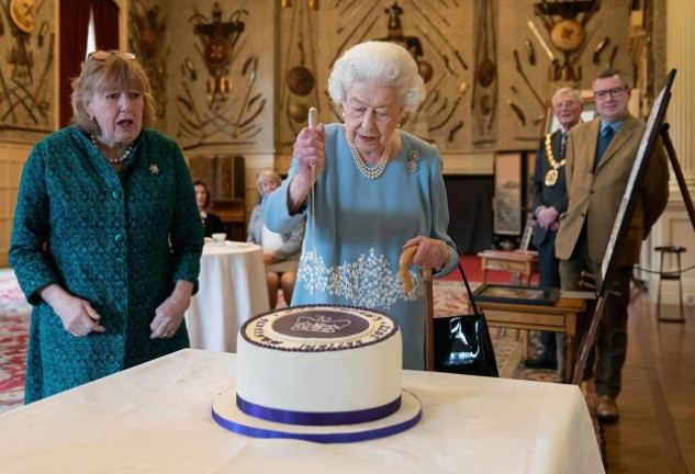 La soberana Isabel II, cortando la tarta ante la mirada atenta de sus asesores. 