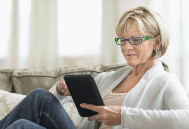 Mature woman using tablet computer while relaxing on sofa at home