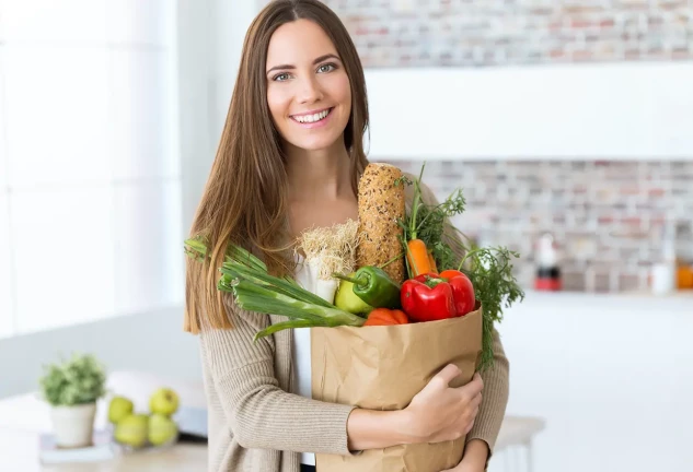Chica sonriente abrazando una bolsa llena de productos frescos comprados en el supermercado