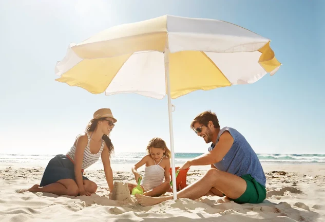 Familia en la playa protegidos del sol por una sombrilla.