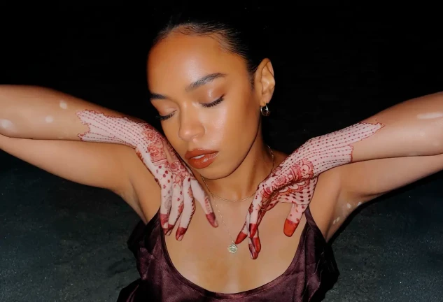Chica con vitiligo y tatuajes de henna en las manos posando con los ojos cerrados