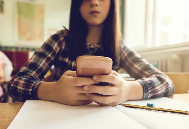 Niña usando un móvil en clase.