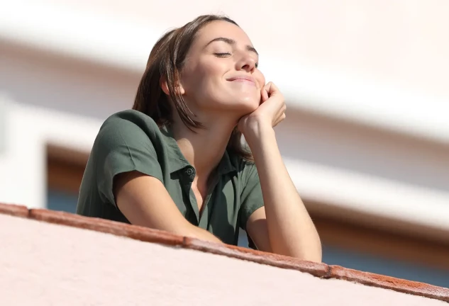 Chica feliz tomando el sol apoyada en la barandilla de un balcón.