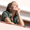 Chica feliz tomando el sol apoyada en la barandilla de un balcón.