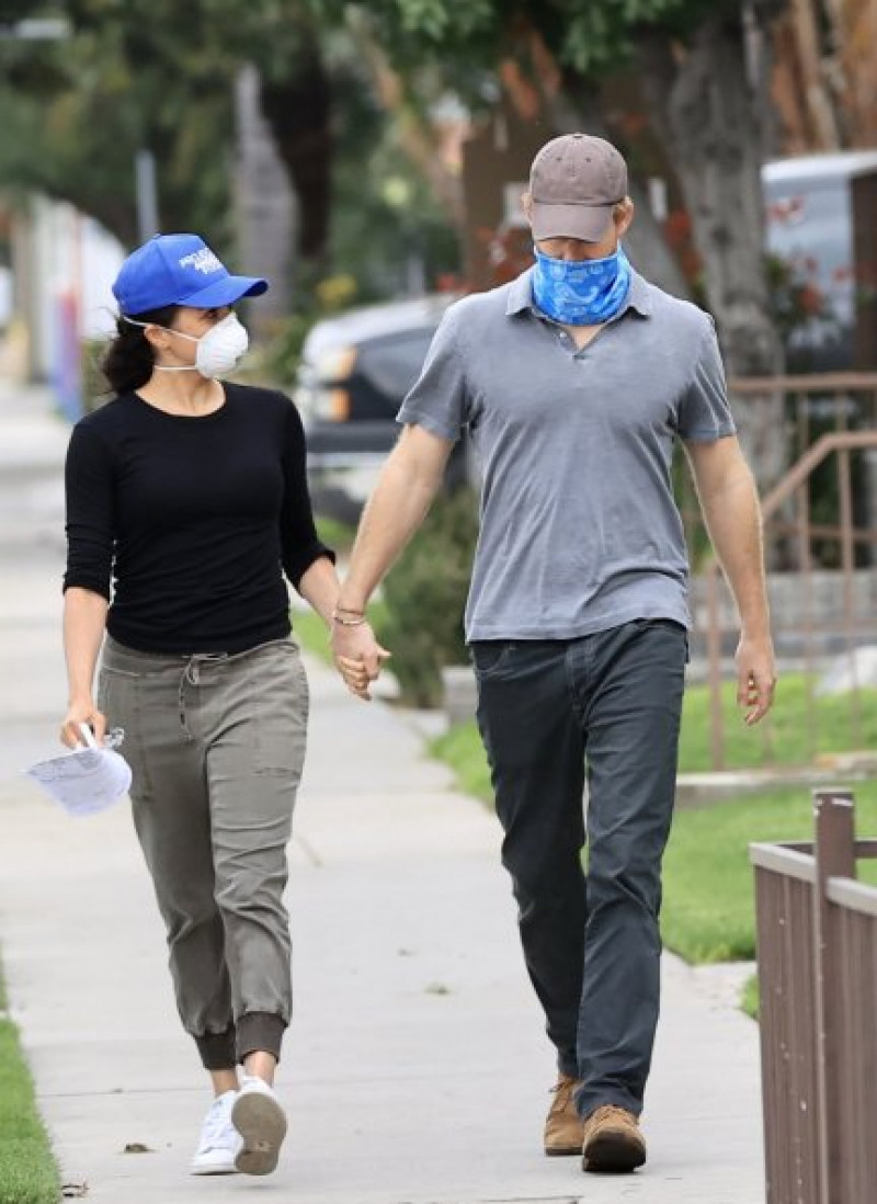 La pareja, de la mano mientras iba de una casa a otra, protegiéndose el rostro para evitar contagios.