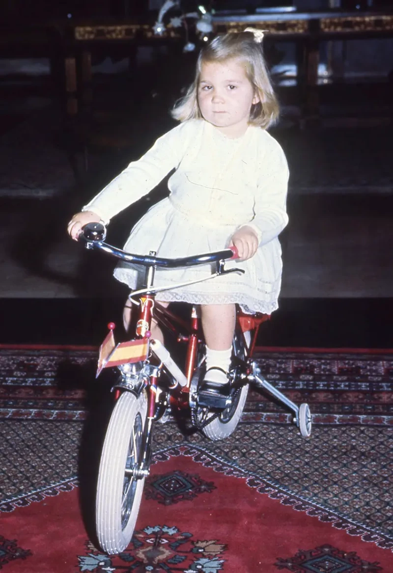 Infanta Elena de niña montada en una bicicleta con ruedines