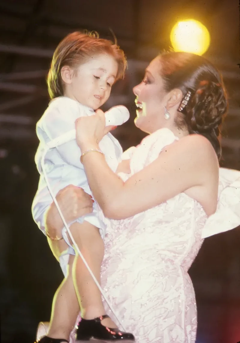 Isabel Pantoja cantándole a su hijo Kiko Rivera sobre un escenario cuando éste era un niño pequeño.