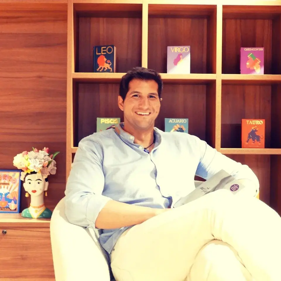 Julián Contreras sonriente sentado en un sillón con una estantería detrás