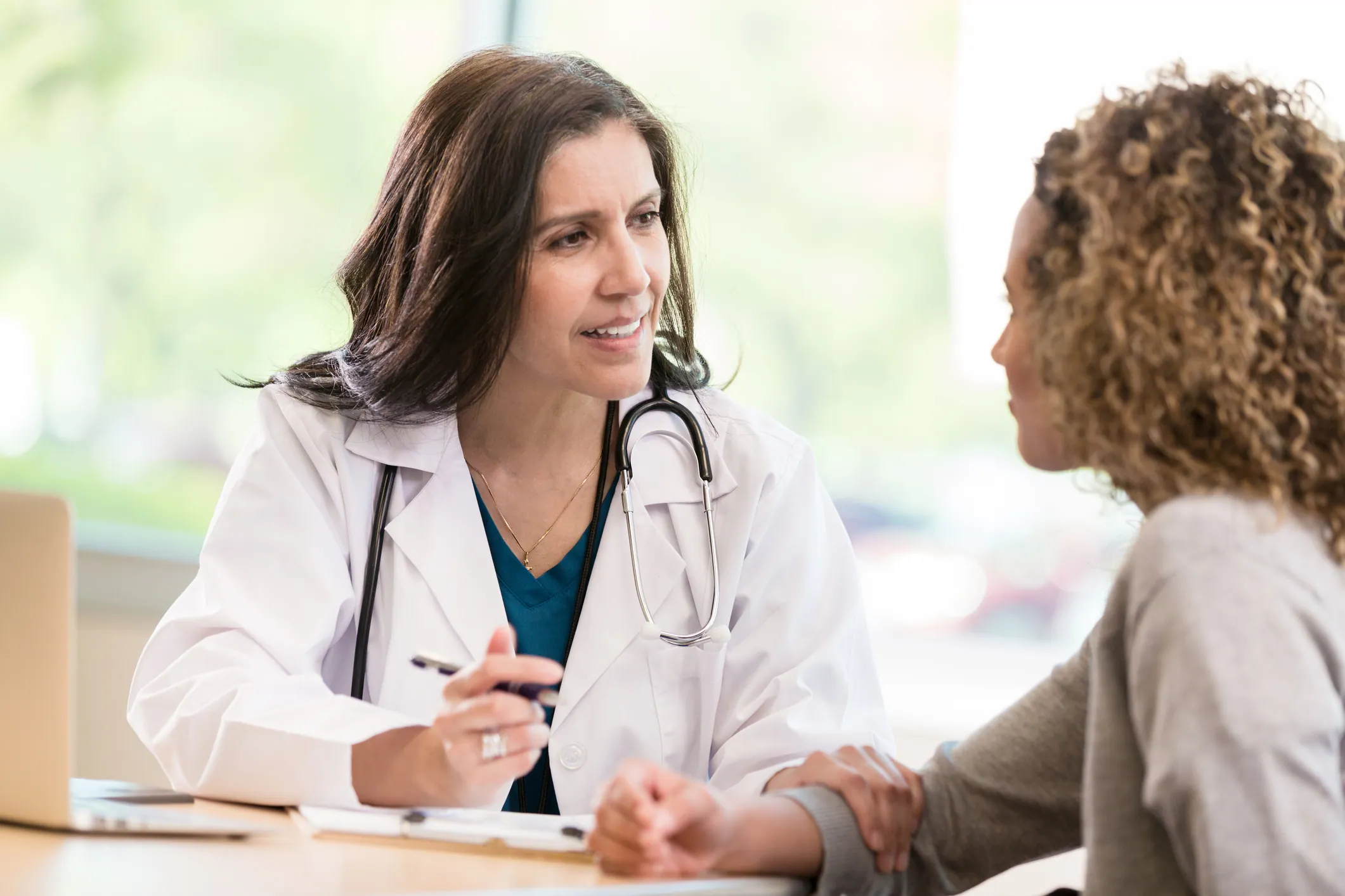 Una doctora madura y atenta pronuncia palabras de consuelo y aliento mientras habla con una paciente adulta joven.