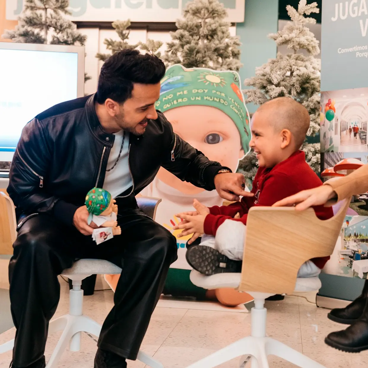 Luis Fonsi saludando a un niño con cáncer con un muñeco Baby Pelón en la mano.