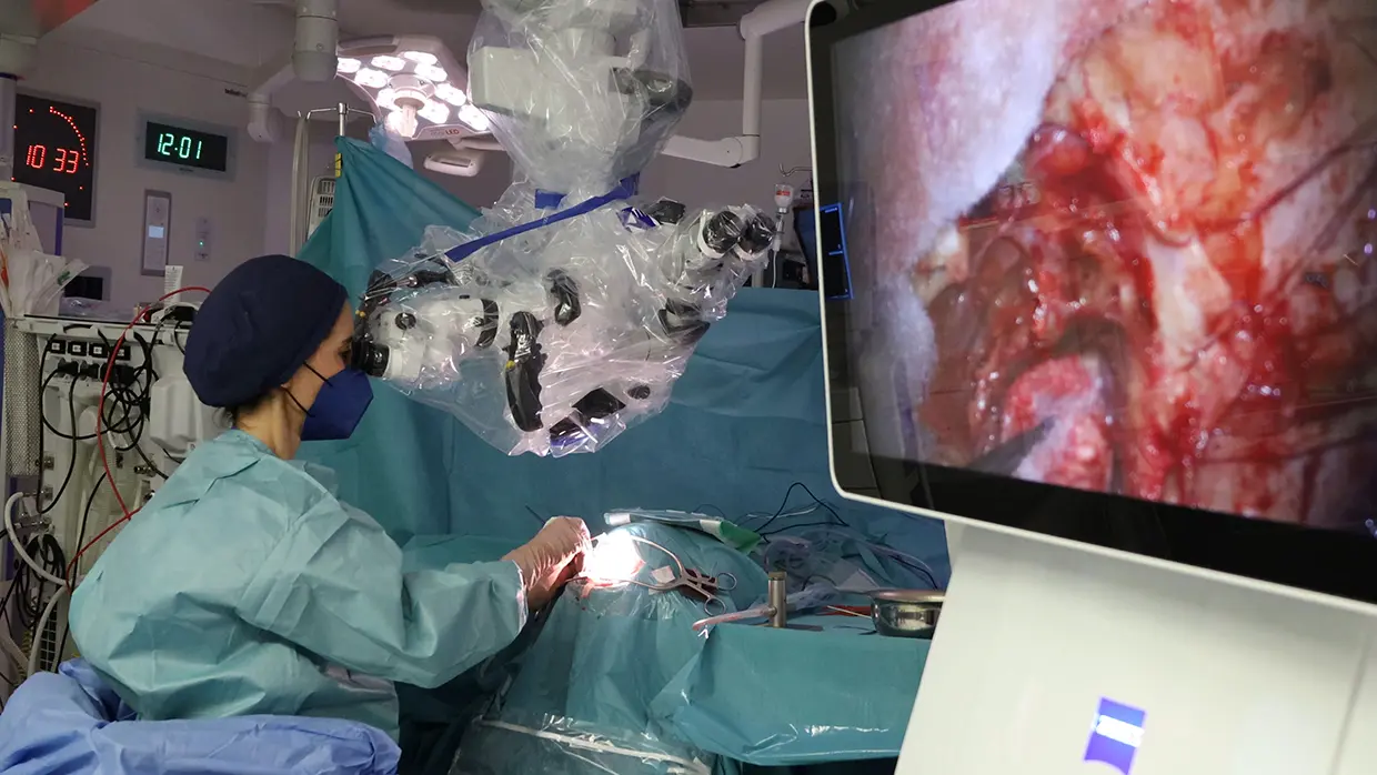 Mujer operando a un paciente a través de un microscopio.