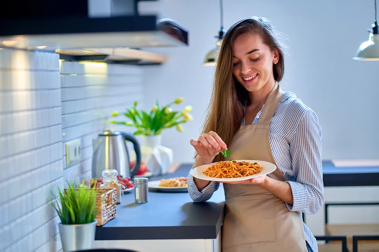 Chica en una cocina con un plato de espaguetis.