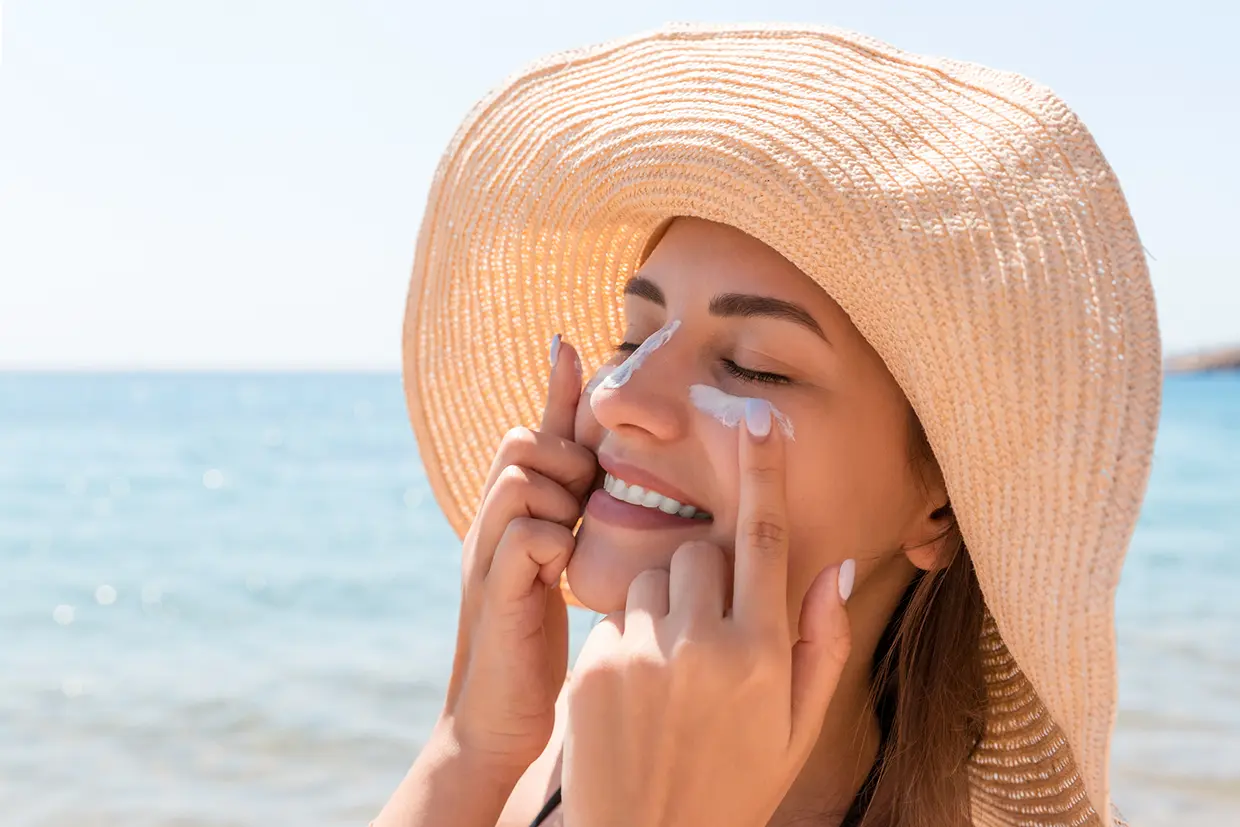 Mujer con sombrero al sol aplicándose crema solar