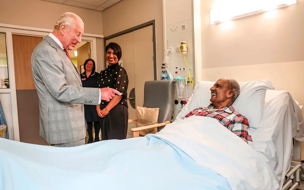 Carlos III de Inglaterra hablando con un hombre enfermo en un hospital